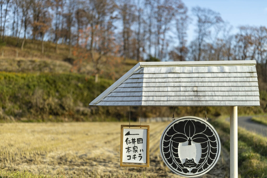 仁井田本家への案内。シンボルマークは、下り藤の家紋に、田んぼの生き物の象徴・カエルがあしらわれている
