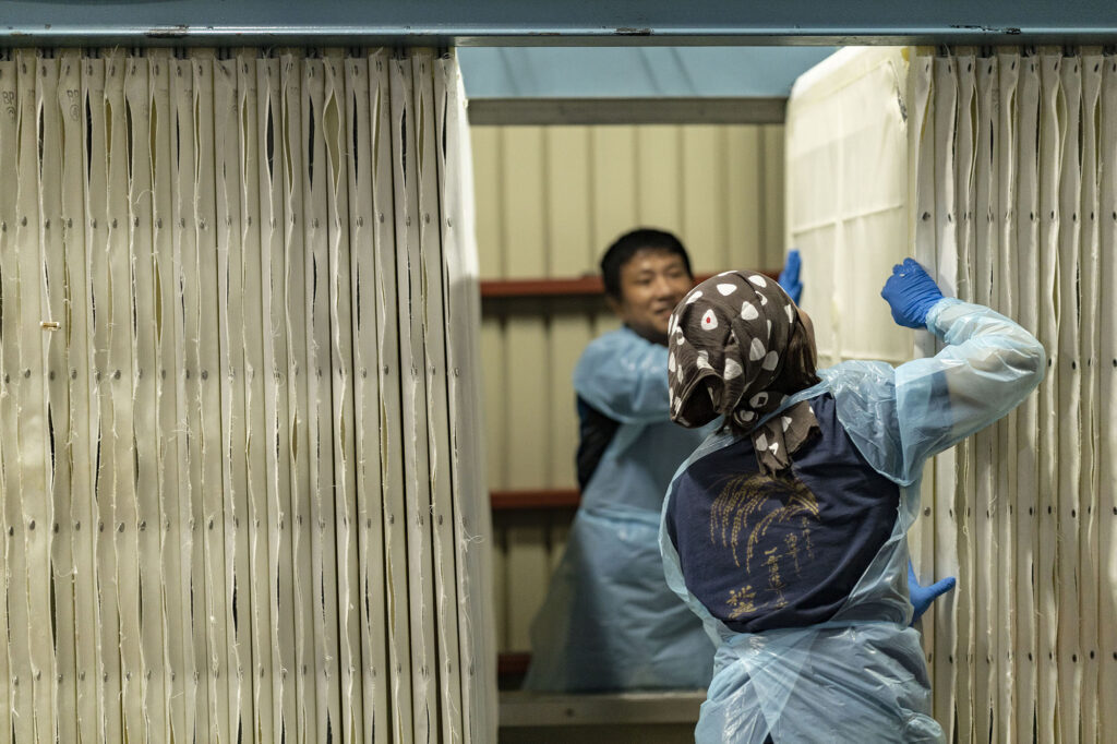 The joso (pressing) process using a 'Yabuta-style' press. The moromi is poured into the white sections seen in the photo, which are composed of plates and filter cloths, and is pressed with pressure from the side. In this step, the sake is separated from the sake-kasu (sake lees).
